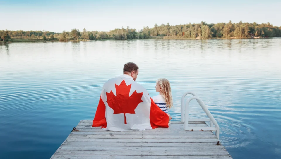 father-daughter-wrapped-canadian-flag-sitting-pier-by-lake-canada-day-celebration-outdoor visa agents in Delhi